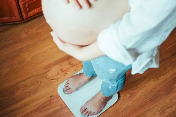 Image of woman weighing herself and experiencing weight gain through pregnancy Walsall